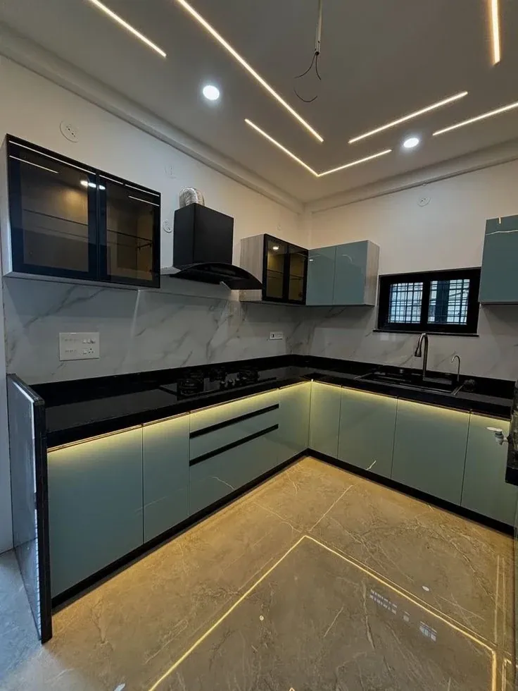 Completed L-shaped kitchen with teal gloss base units, warm plinth lighting, black counter and black glass-fronted wall cabinets